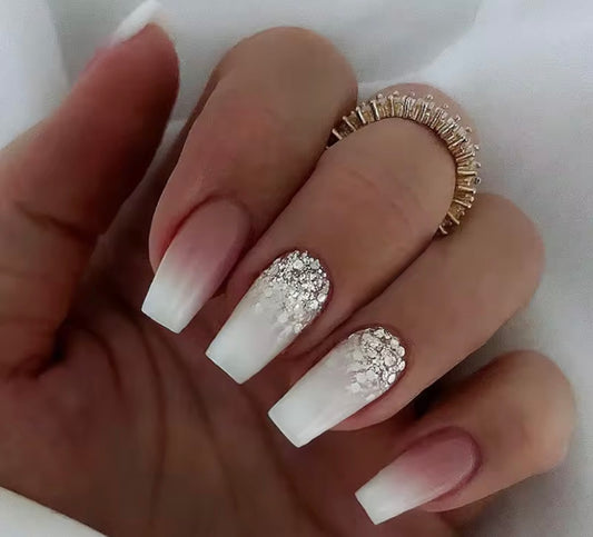 Hand with white nails and silver glitter design, wearing a gold ring on a white background